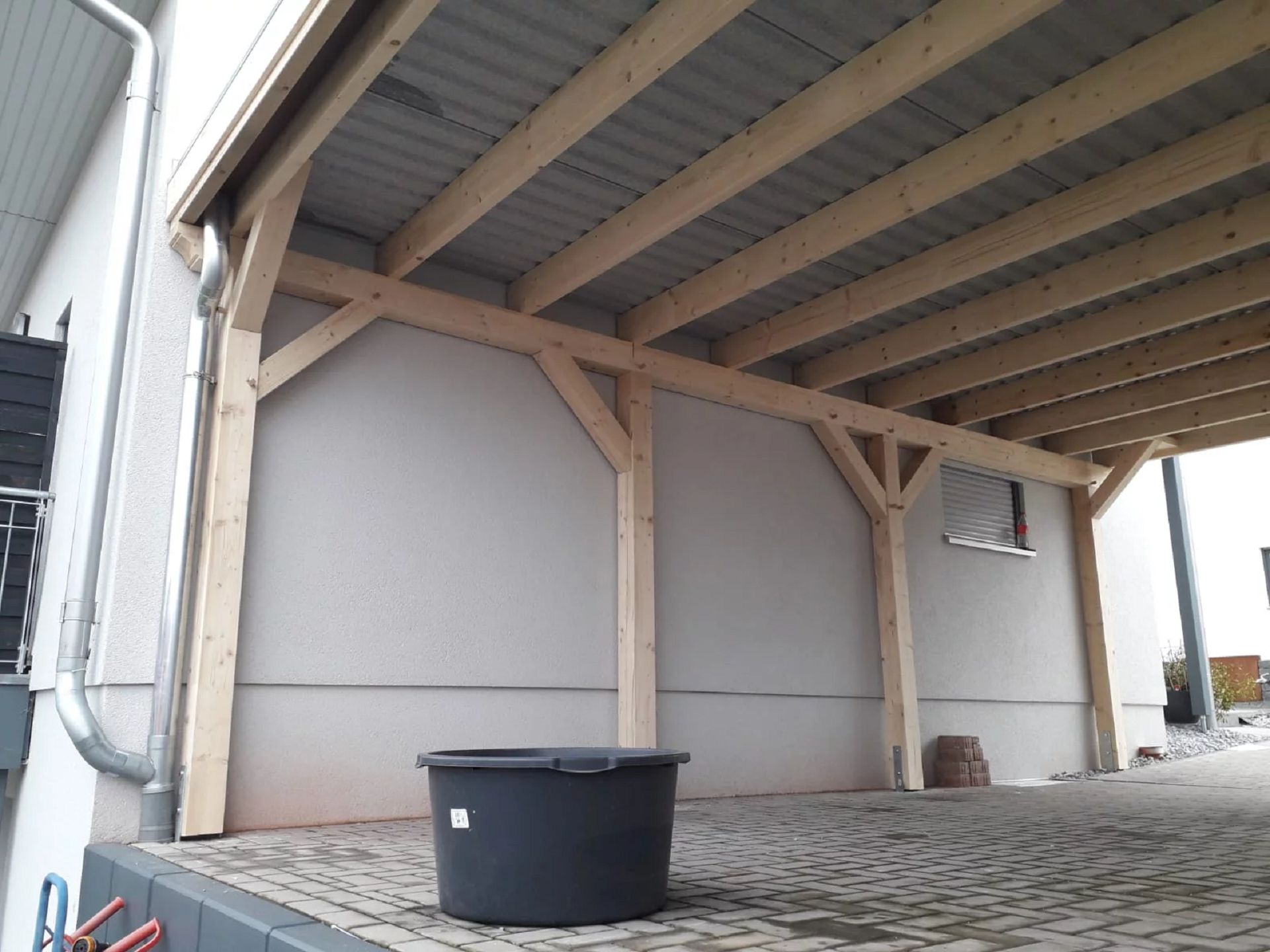 Innenansicht auf die Konstruktion eines Doppelcarports mit Flachdach. Im Vordergrund steht ein schwarzer Eimer.