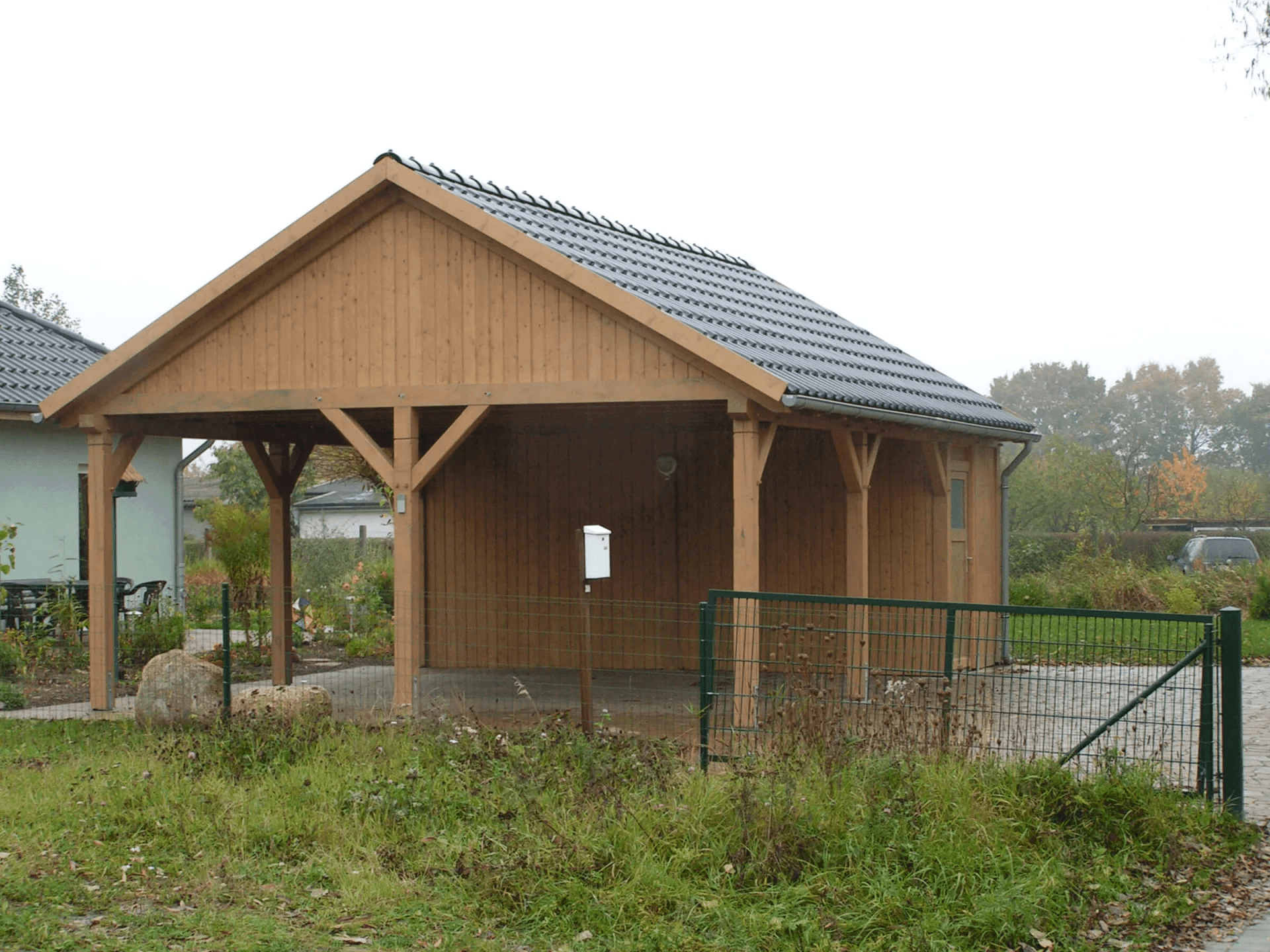 Freistehender Doppelcarport aus Holz, das neben einem Wohnhaus steht. Der Carport bietet Platz für zwei PKW. Im hinteren Teil des Carports befindet sich ein kleiner Geräteraum.