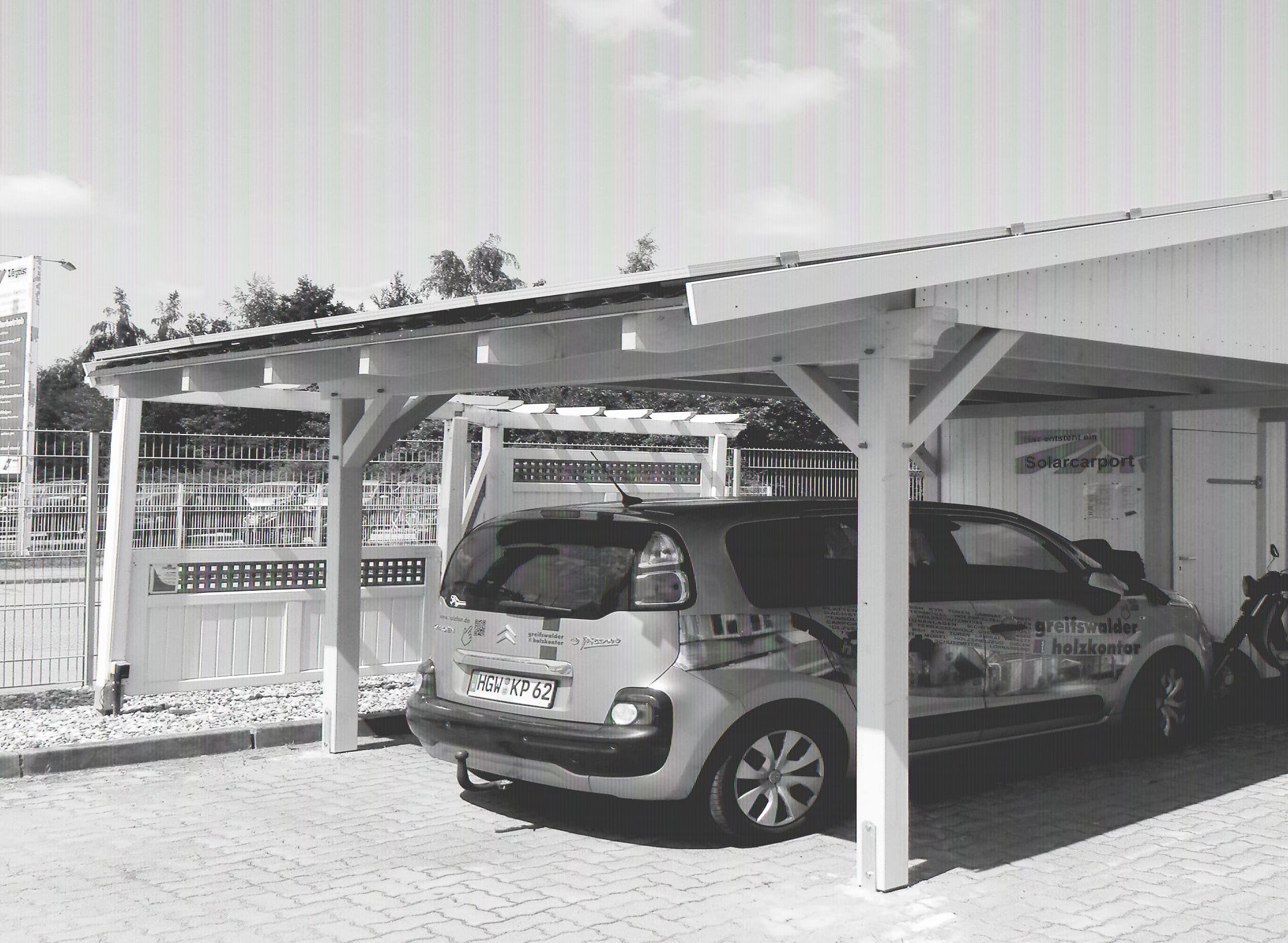 Grüner PKW parkt unter einem Einzelcarport aus Holz. Auf dem Dach des Carports befinden sich einige Solarpanels.