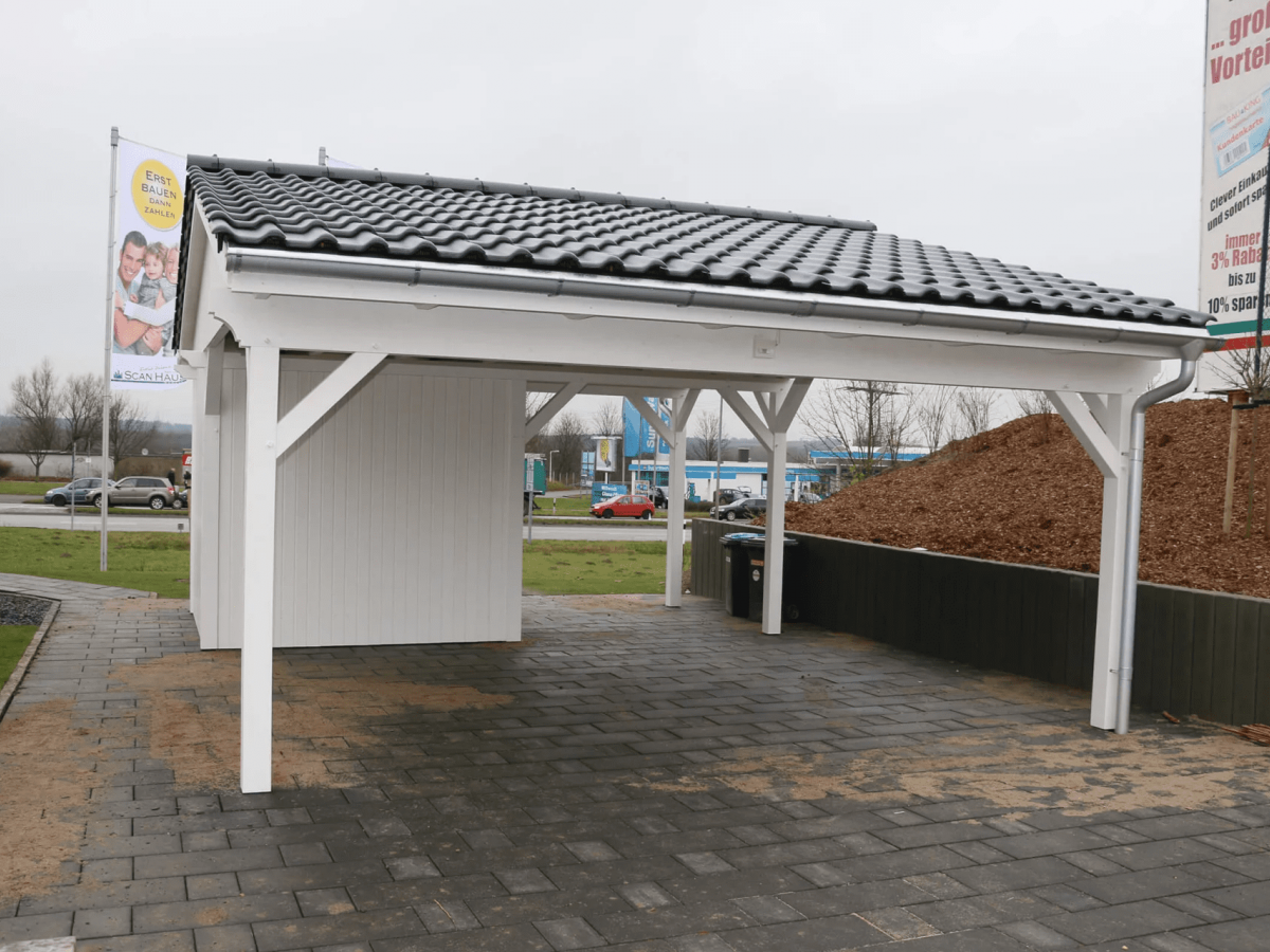 Einfahrt auf das Grundstück, auf dem ein großer Doppelcarport steht. Das Holz des Carports ist weiß gestrichen und das Satteldach verfügt über dunkelgraue Dachziegel.
